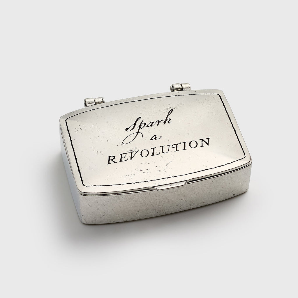 Silver matchbox with 'Spark a Revolution' text on a white background